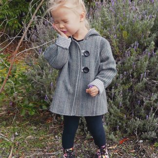 Child wearing the Baby/Child Awhi Coat sewing pattern from Below the Kōwhai on The Fold Line. A coat pattern made in wool, melton cloth or upcycled blnkets fabrics, featuring a cross-over front, gusset style hood, in-seam pockets and button and loop fastening.