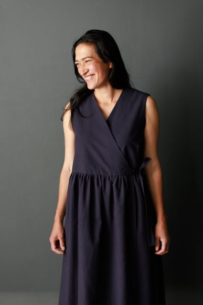Woman wearing The Etta Dress sewing pattern from Merchant & Mills on The Fold Line. A sleeveless, wrap dress pattern made in linen, brushed cotton, cotton lawn, cotton poplin, tencel, Indian handlooms, lightweight baby cord or cotton double gauze fabrics featuring a lined bodice, in-seam pockets, relaxed fit, fabric side tie and midi length.