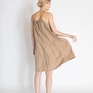 Woman wearing the Greta Dress sewing pattern from Bara Studio on The Fold Line. A sun dress pattern made in cotton, linen or tencel fabrics, featuring a loose wide fit, thin shoulder straps, side slits, neckline gathers, back neck bow closure and knee length hem.