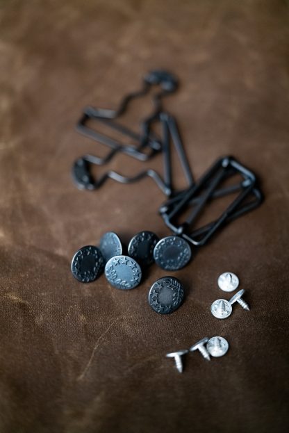 Photo showing the Harlene Hardware Kit for the Harlene Dungarees from Merchant & Mills on The Fold Line. A hardware kit containing metal sliders and clips plus hammer-in jeans buttons which are plastic inside with a metal outer.