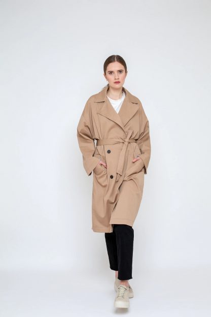 Woman wearing the Kara Trench Coat sewing pattern from Bara Studio on The Fold Line. A trench coat pattern made in cotton, linen or tencel fabrics, featuring an oversized fit, loose drape, dropped shoulders, front button closure, front pockets, tie belt, collar and stand.