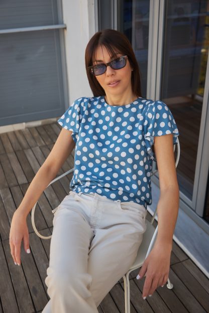 Woman wearing the Lily Top sewing pattern from The Patterns Room on The Fold Line. A top pattern made in viscose, cotton voile, crepe or georgette fabrics, featuring a relaxed fit, round neck, ruffled short sleeves, waistband which is tied at the back leaving a slit opening and small gathers on the sleeves and waistband.