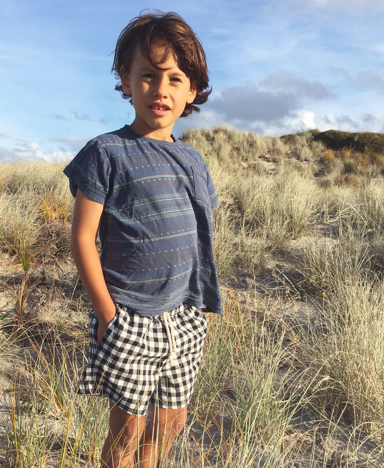 Child wearing the Pai Shorts sewing pattern from Below the Kōwhai on The Fold Line. A shorts pattern made in cotton, poly cotton, linen or chambray fabrics featuring a relaxed fit, above knee length, enclosed elastic waistband, drawstring and in-seam pockets.