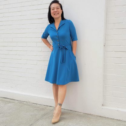 Woman wearing the Marianne Dress sewing pattern from Wardrobe by Me on The Fold Line. A dress pattern made in light to medium weight jersey fabrics, featuring front buttons, A-line skirt, self-fabric belt, in-seam pockets, fitted bodice, front and back darts, V-neck with pointed shawl collar and knee length hem.