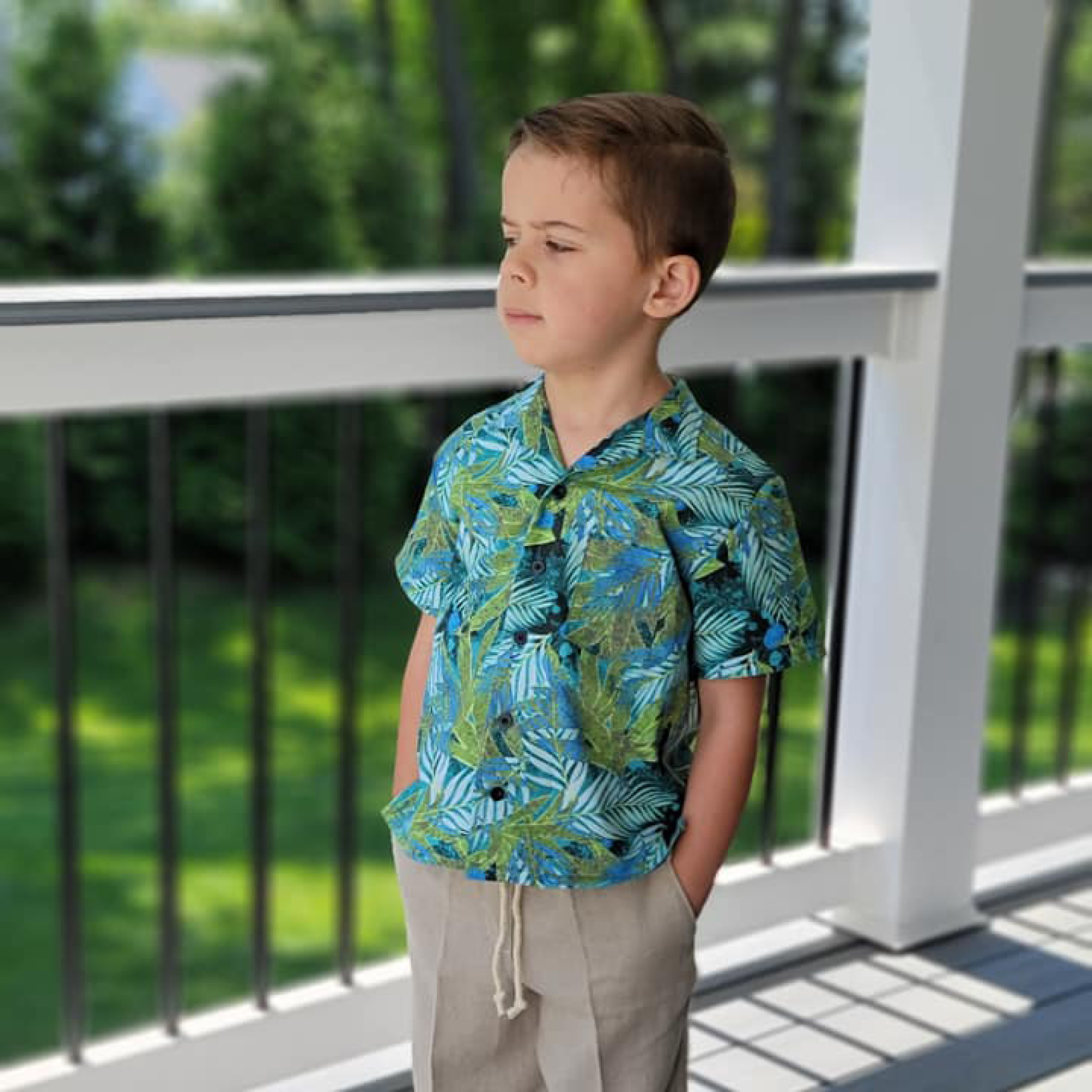 Child wearing the Children's Tropical Shirt sewing pattern from Wardrobe by Me on The Fold Line. A shirt pattern made in cotton, viscose or linen fabrics, featuring front button closure, short-sleeves, convertible collar, double yoke, two back pleats, side slits and left front breast pocket.