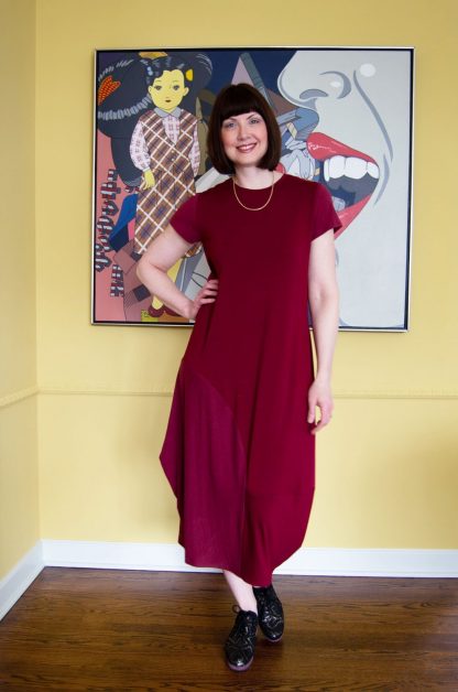 Woman wearing the Edgewater Dress sewing pattern from The Sewing Workshop on The Fold Line. A dress pattern made in two-way and four-way light to mid weight knit fabrics, featuring a semi-fit, mid-calf length, crew neck, short sleeves, asymmetric bottom panels and side dart.