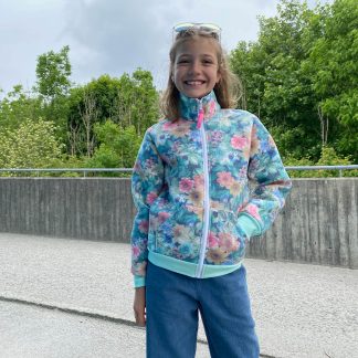 Child wearing the Children's Zipper Jacket sewing pattern from Wardrobe by Me on The Fold Line. A jacket pattern made in medium weight french terry, scuba or sweatshirt fleece fabrics, featuring a front zipper, kangaroo pockets, high funnel neck, ribbed hem and cuffs and casual fit.