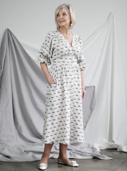 Woman wearing the Belle Woven Dress sewing pattern from Style Arc on The Fold Line. A dress pattern made in crepe, silk or rayon fabrics, featuring a V-neck, front button closure, shirred sleeves with elastic opening, back waist shirring, gathered bodice, skirt and sleeve heads, double front waist yoke, midi length and in-seam pockets.