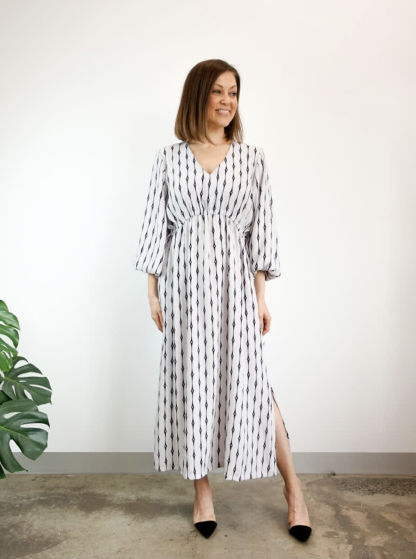 Woman wearing the Naomi Woven Dress sewing pattern from Style Arc on The Fold Line. A dress pattern made in silk, crepe or rayon fabrics, featuring a slip-on longline style, V-neck, angled waist seam with drawstring, 7/8-length sleeves with elastic cuffs, midi length and side splits.