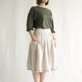Woman wearing the Richmond Utility Skirt sewing pattern from Style Arc on The Fold Line. A skirt pattern made in washed linen, poplin or crepe fabrics, featuring front and back topstitched box pleats, pockets with centre box pleat, side seam invisible zip, hem facing, hem tie, just below knee length and sits on the natural waistline.