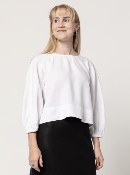 Woman wearing the Verona Woven Top sewing pattern from Style Arc on The Fold Line. A top pattern made in linen or cotton fabrics, featuring a pull-on style, square-shaped body, high hip length, raglan 3/4-length bias-cut sleeves with elastic cuff, gathered front and back neck, bound neckline, button-and-loop opening and wide hem facing.