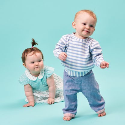 Babies wearing the Babies' Clover Reversible Trousers sewing pattern from Poppy & Jazz on The Fold Line. A trouser pattern made in cotton lawn, poplin, linen or corduroy fabrics, featuring a reversible style, elasticated waist, full length leg with contrasting elasticated ankle band.