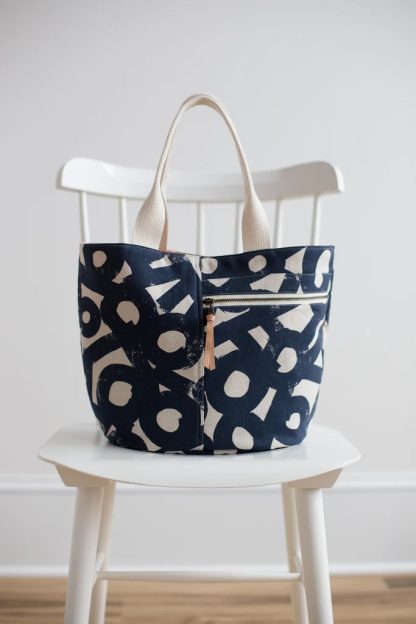 Photo showing the Crescent Tote sewing pattern from Noodlehead on The Fold Line. A tote pattern made in canvas fabrics, featuring a small size, zippered front pocket, internal zipped pocket, flat bottom, carry handles.