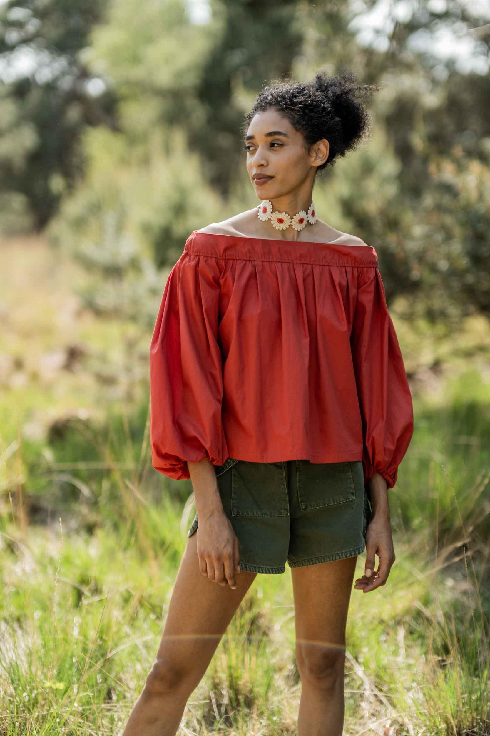 Woman wearing the Lia Top sewing pattern from Fibre Mood on The Fold Line. A top pattern made in silk satin, double gauze, viscose crepe, or muslin fabrics, featuring an off-the-shoulder silhouette, fitted above the bust then gathered with knife pleats, sleeves have a curved hemline being shorter at the front.
