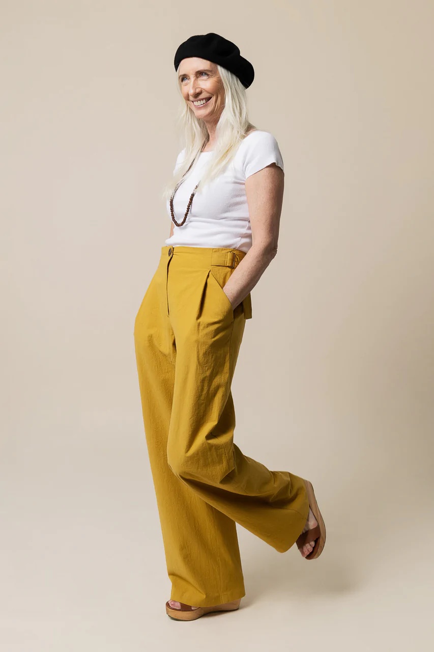 Woman wearing the Mitchell Trousers sewing pattern from Closet Core Patterns on The Fold Line. A trouser pattern made in denim, twill, canvas, linen, cotton or wool suiting fabrics, featuring a high waist, fly front zip and button closure, deep front pleats, angled pockets, back darts, back welt pockets, full-length wide legs and adjustable waist straps secured with D-rings.
