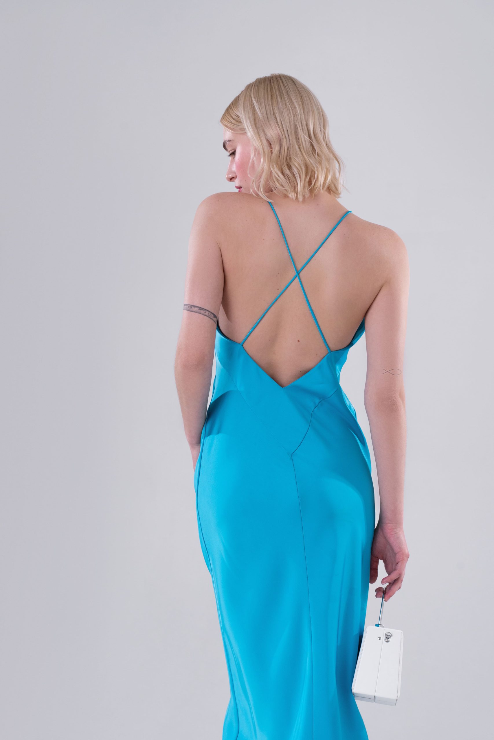 Woman wearing the Lucia Dress sewing pattern from Vikisews on The Fold Line. A slip dress pattern made in silk, artificial silk, dress-weight viscose, crepe back satin or challis fabrics, featuring a close fit, bias cut, centre back seam, bust darts, spaghetti straps criss-crossing at the back, open back V cut and midi length.