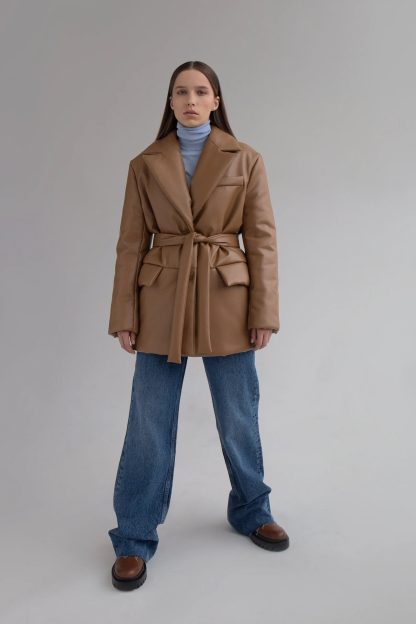 Woman wearing the Aurelia Jacket sewing pattern from Vikisews on The Fold Line. A single-breasted jacket pattern made in PU leather or blended raincoat fabrics, featuring a loose fit, straight silhouette, bust darts, built-in pockets with flaps, faux welt chest pocket, two-piece sleeve, notched collar with stand, centre front button fastening, separate tie belt and below-the-hip length.