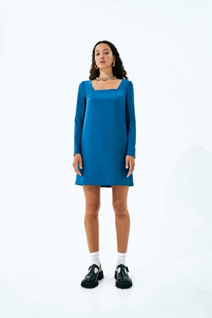Woman wearing the Becky Dress sewing pattern from Vikisews on The Fold Line. A dress pattern made in dress-weight suiting, dress-weight wool, wool crepe or gabardine fabrics, featuring a semi-fitted trapeze style, free-hanging lining, deep square neckline, invisible centre back zipper, bust darts, back shoulder darts, long set-in sleeves and above-knee length.