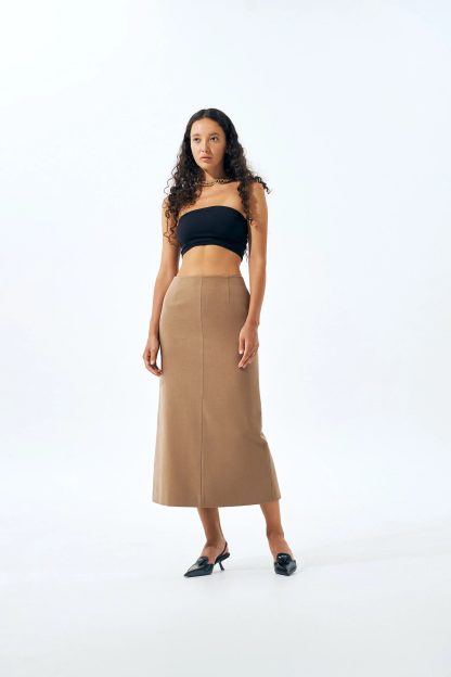 Woman wearing the Blake Skirt sewing pattern from Vikisews on The Fold Line. A skirt pattern made in dress-weight suiting or suiting fabrics, featuring a semi-fit, slightly flared with straight silhouette, no separate waistband, front and back waist darts, invisible zipper, slit in the centre back seam, side seam pockets, free-hanging lining and midi length.
