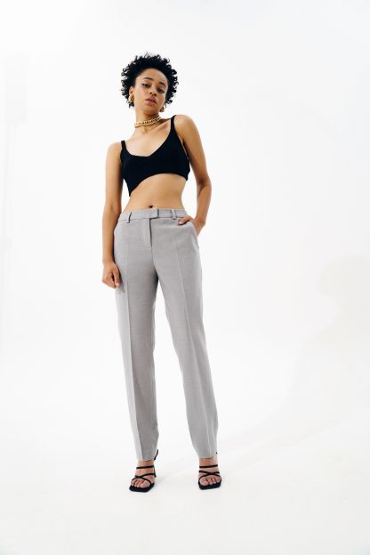 Woman wearing the Edna Trousers sewing pattern from Vikisews on The Fold Line. A trouser pattern made in wool suiting or gabardine fabrics, featuring a straight-cut, close-fit, slightly tapered, front and back pressed creases, front slash pockets, back welt pocket, back waist darts, three-piece waistband, belt loops, fly front zipper closure and ankle-length.