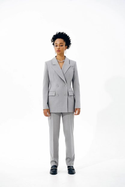 Woman wearing the Fernanda Blazer sewing pattern from Vikisews on The Fold Line. A blazer pattern made in wool suiting or gabardine fabrics, featuring a semi-fit, lined, accentuated waist, shoulder and waist darts, vertical bust darts, welt pockets, long set-in sleeves, turned-down notched collar with collar stand, double-breasted button and buttonhole closure and is below-hip length.