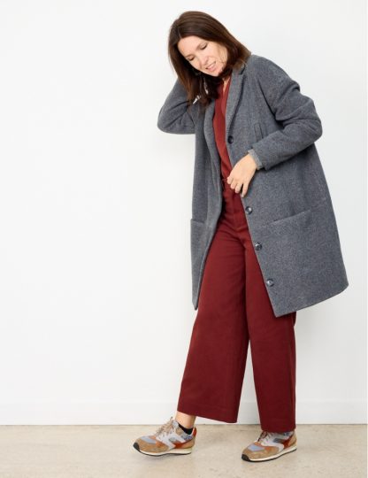 Woman wearing the Flow Coat or Jacket sewing pattern from Atelier Scämmit on The Fold Line. A coat pattern made in woollen or jacquard fabrics, featuring an oversized silhouette, slight round shape, dropped shoulders, tailored collar, pockets, front button closure and knee length finish.