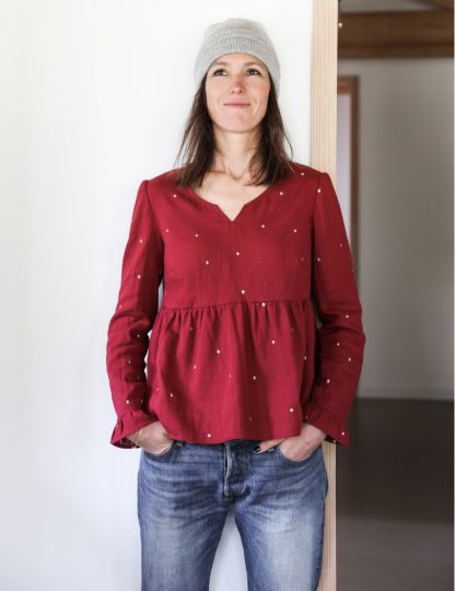 Woman wearing the Pepa Blouse sewing pattern from Atelier Scämmit on The Fold Line. A blouse pattern made in batiste, crepe, double gauze, or light denim fabrics, featuring a round neckline with small V notch, button back closure, long sleeves with gathered flounce hem and gathered peplum.