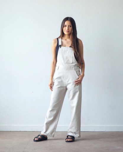 Woman wearing the Riley Overalls sewing pattern from True Bias on The Fold Line. A dungarees pattern made in denim, corduroy, twill or linen fabrics, featuring a relaxed fit, two hem lengths, shoulder straps, front bib with patch pockets, rear patch pockets, belt loops and a faux fly.