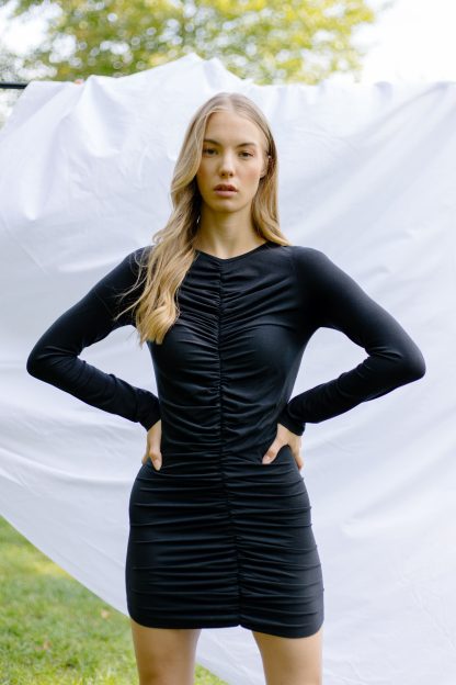 Woman wearing the Tia Dress sewing pattern from JULIANA MARTEJEVS on The Fold Line. A knit dress pattern made in cotton jersey fabrics, featuring long sleeves, round neckline, close fit, mini length and full length gathered centre front.