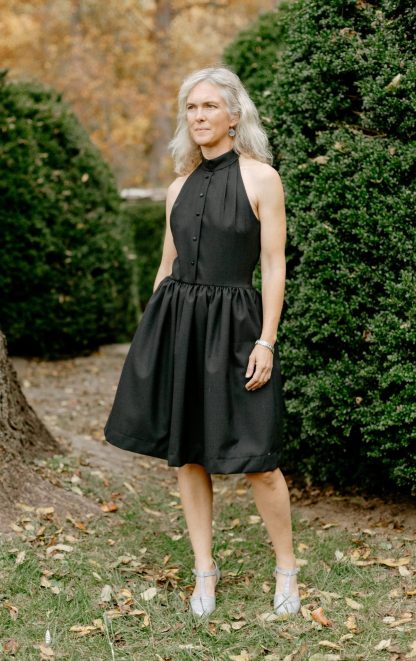 Woman wearing the 258 Town and Country Dress sewing pattern from Folkwear on The Fold Line. A dress pattern made in medium-weight cotton, rayon, silk, wool challis, or blends fabrics, featuring a high halter neck, gathered skirt, button front bodice, side zip, in-seam pockets, knee length and cold shoulders.