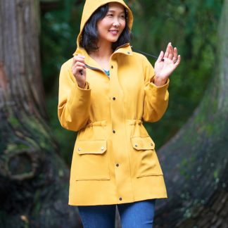 Woman wearing the Winterthur Jacket sewing pattern from Itch to Stitch on The Fold Line. A lined jacket pattern made in Twill, broadcloth, chambray, taslan nylon or linen fabrics, featuring front princess seams, back yoke, drawstring waist, front patch pockets, front zipper with buttoned flap, three-piece hood, long sleeves with snap closure and mid-thigh length.