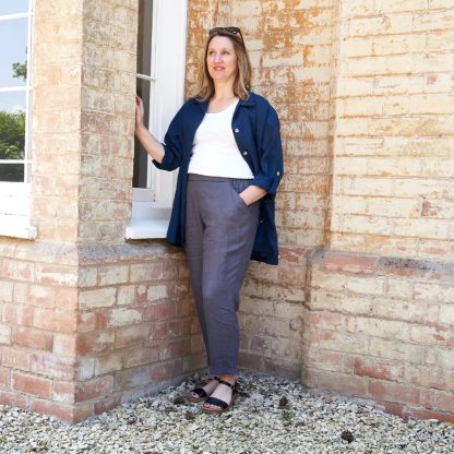 Woman wearing the Nell Trouser sewing pattern from Sew Me Something on The Fold Line. A trouser pattern made in linen, chambray, ramie, viscose rayon, denim, corduroy, or cotton drill fabrics, featuring a relaxed fit, pull-on style, slim leg, flat front waistband, elasticated back waistband, front cut-away pockets, back patch pockets and ankle skimming length.