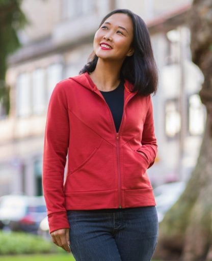 Woman wearing the Nazare Zip-up Hoodie sewing pattern from Itch to Stitch on The Fold Line. A hoodie pattern made in sweatshirting, French terry, jersey, interlock and double-brushed poly fabrics, featuring diagonal front seams, hood, large patch pockets with curved openings, exposed front zipper, long sleeves with cuffs and hem band.