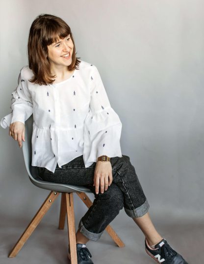 Woman wearing the Tiered Blouse sewing pattern from The Maker's Atelier on The Fold Line. A blouse pattern made in lightweight shirting fabrics, cotton voiles, Tana lawn and fine linen fabrics, featuring a relaxed fit, front button closure, round neck, voluminous tiered sleeve and gathered waist tier.
