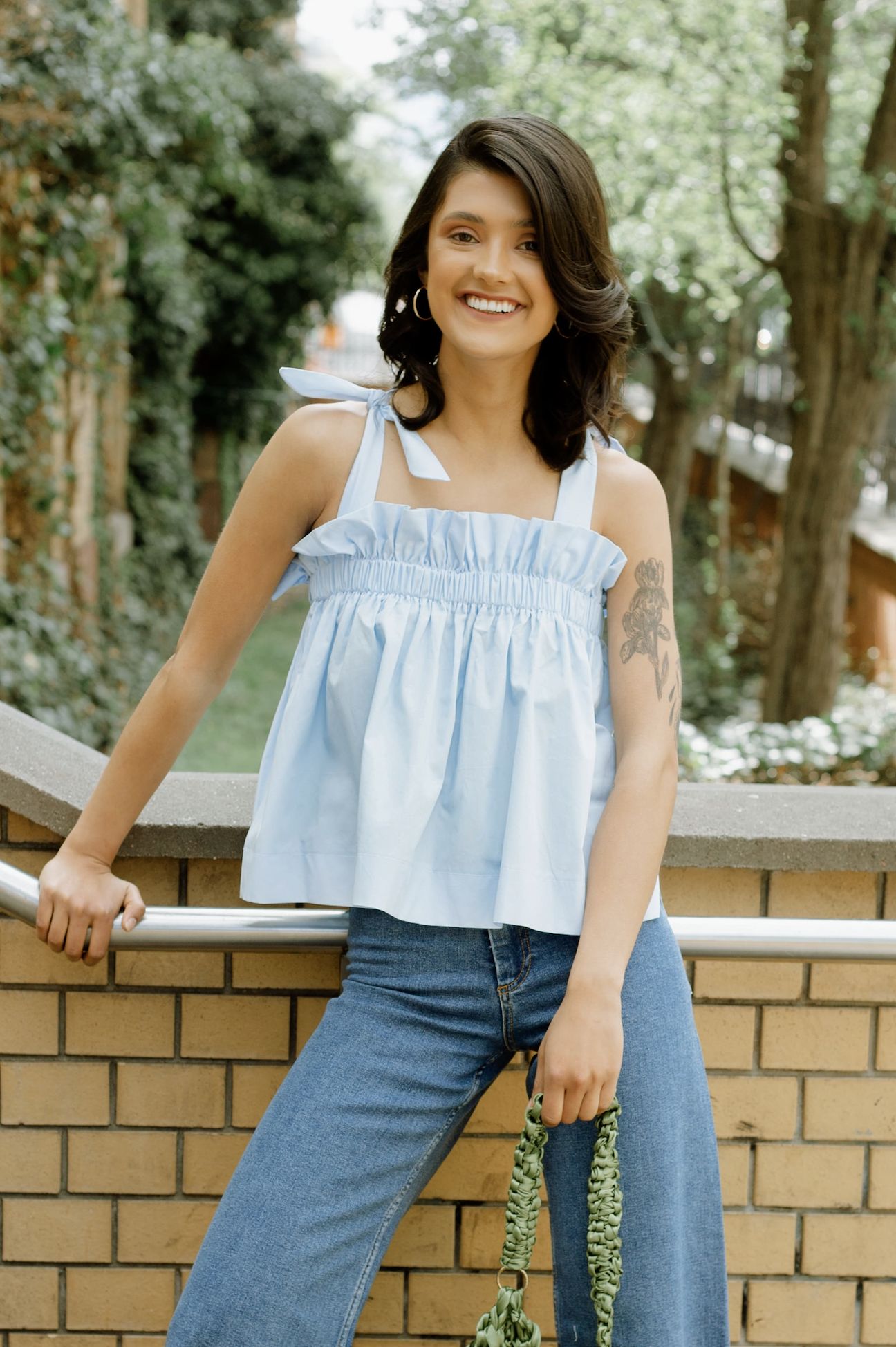 Woman wearing the Judy Blouse sewing pattern from JULIANA MARTEJEVS on The Fold Line. A baby doll top pattern made in cotton poplin fabrics, featuring tie shoulder straps crossed at the back, elasticated, front and back chest ruffle, and relaxed fit.