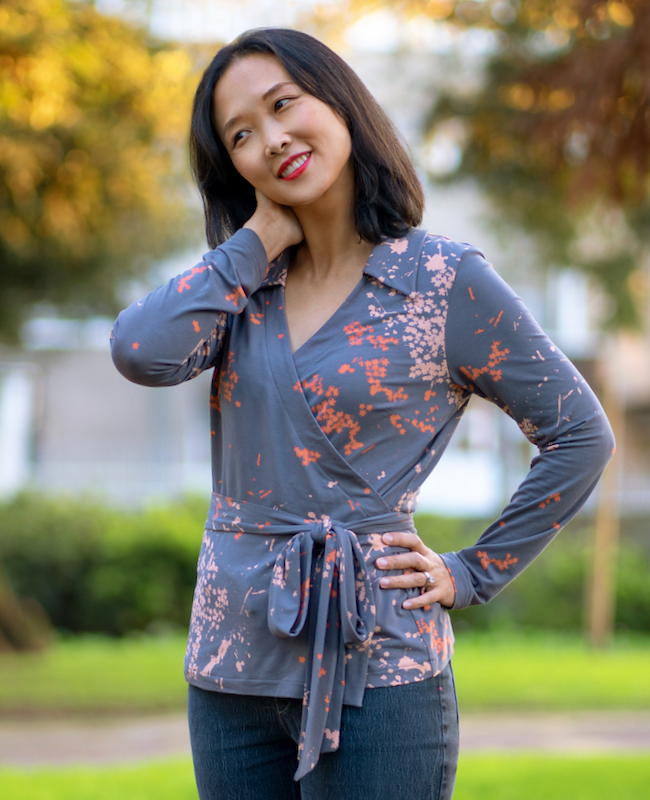 Woman wearing the Coimbra Wrap Top sewing pattern from Itch to Stitch on The Fold Line. A wrap top pattern made in jersey, French terry, interlock and double-brushed poly fabrics, featuring a V-neck, waist tie, bust darts, collar, and full-length sleeves.
