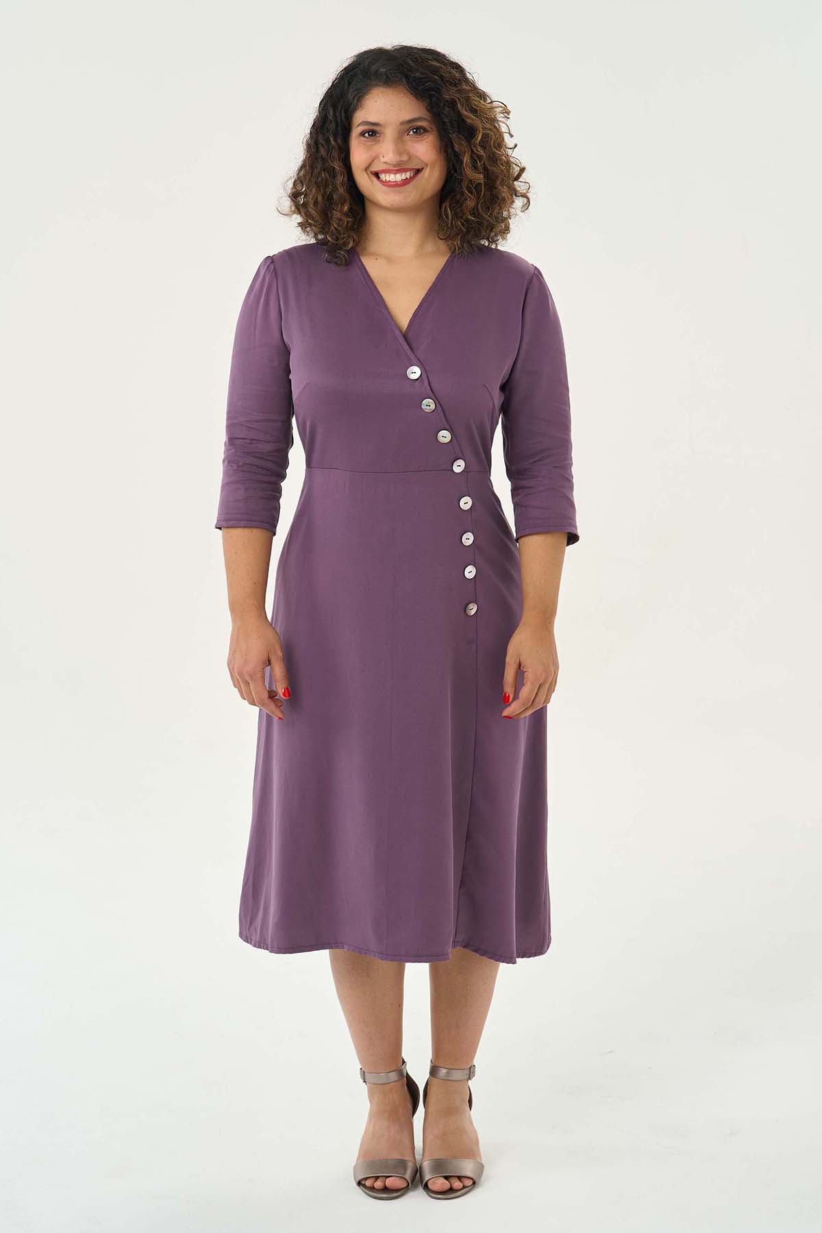 Woman wearing the Pippa Dress sewing pattern from Sew Over It on The Fold Line. A dress pattern made in rayon, viscose and crepe fabrics, featuring a front asymmetrical line of buttons, bust darts, back bodice waist darts, side invisible zip closure, V-neckline, ¾ length sleeves, and midi length.