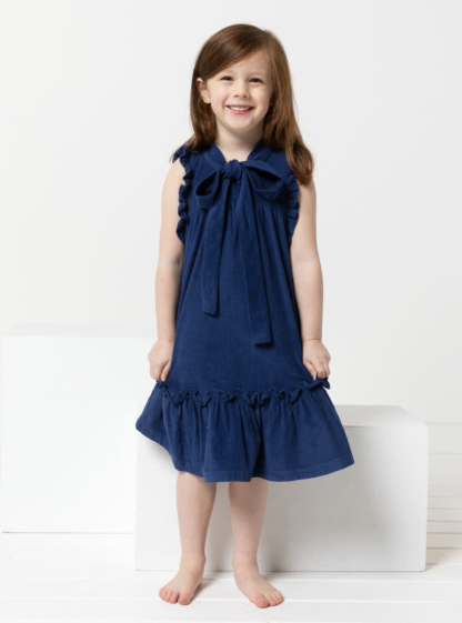 Child wearing the Children's Bonnie Dress sewing pattern from Style Arc on The Fold Line. A dress pattern made in linen, rayon, or cotton fabrics, featuring an A-line swing shape, front and back yokes, gathered armhole and hem frills, neck tie and back neck button-and-loop closure.