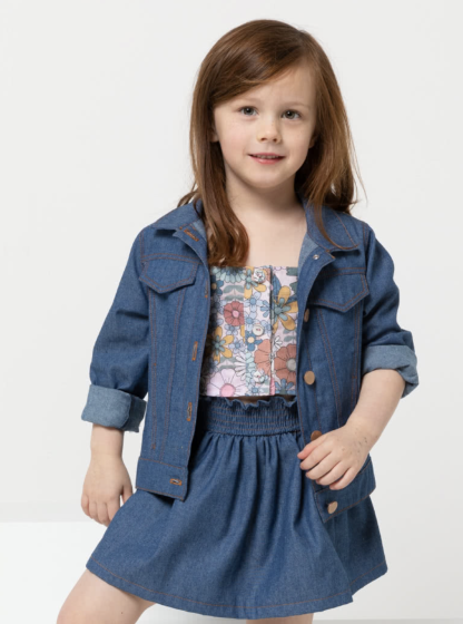 Child wearing the Children's Charlie Jacket sewing pattern from Style Arc on The Fold Line. A denim jacket pattern made in denim, cotton drill, or heavy linen fabrics, featuring in-seam pockets, detachable hood or collar, front and back yoke, full length sleeves with button cuffs, front button closure, and top stitching.