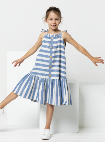 Child wearing the Children's Claudia Dress sewing pattern from Style Arc on The Fold Line. A dress pattern made in rayon, linen or cotton fabrics, featuring an A-line shape, spaghetti strap ties, front and back neck ruffle, hem frill, knee length, and faux button front.
