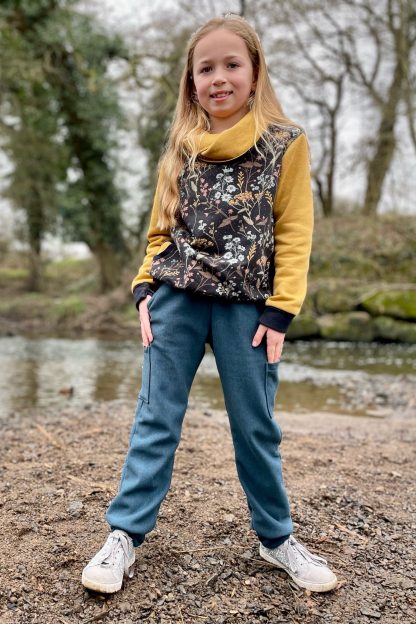Child wearing the Baby/Child Field Trip Joggers sewing pattern from Waves & Wild on The Fold Line. A joggers pattern made in stretch knit fabrics, featuring a relaxed fit, hip pockets, patch pocket and elasticated waist.