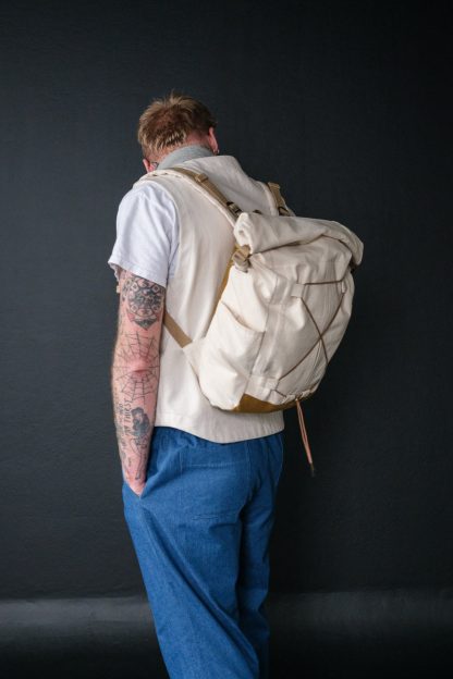 Man wearing the Francli Day Pack sewing pattern from Merchant & Mills on The Fold Line. A back pack pattern made in oilskin, dry oilskin, cotton canvas, drill, or mid weight denim fabrics, featuring water bottle pockets, internal laptop pocket, adjustable shoulder straps, and fold-over top.