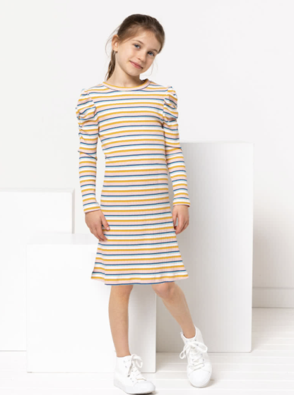 Child wearing the Children’s Issy Knit Dress sewing pattern from Style Arc on The Fold Line. A Knit Dress pattern made in stretch knit rib fabrics, featuring a scoop neckline, long sleeves with ruching, and knee length hem.