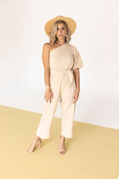 Woman wearing the Jacky Jumpsuit sewing pattern from Pattern Sewciety on The Fold Line. A jumpsuit pattern made in cotton, linen or rayon fabrics, featuring an asymmetrical neckline, cold shoulder, short puff sleeve, front and back waist darts, side invisible zip, cropped length, in-seam pockets, and self-fabric belt.