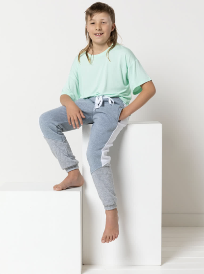 Child wearing the Child/Teen Riley Sweatpant sewing pattern from Style Arc on The Fold Line. A sweatpant pattern made in fleece, jersey, or sweater knit fabrics, featuring an elasticated waist and cuffs, non-functional shoelace waist tie, in-seam pockets, and side leg panels.