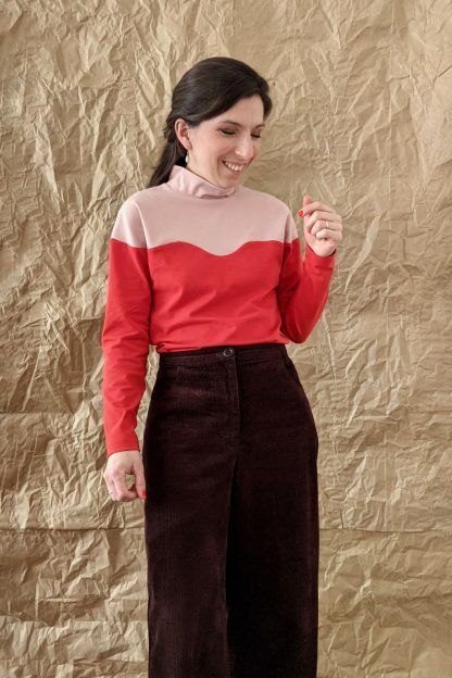Woman wearing the Vague Top sewing pattern from Camimade on The Fold Line. A top pattern made in cotton jersey or sweatshirt fabrics, featuring long batwing sleeves, high neck, curved seamline across chest and shoulders, and colour blocked.