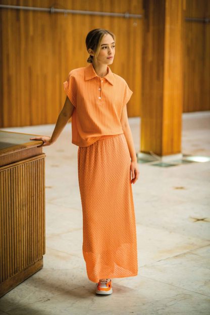 Woman wearing the Amber Top sewing pattern from Fibre Mood on The Fold Line. A top pattern made in piqué, (ribbed) jersey, jacquard jersey, French terry, or interlock fabrics, featuring a straight fit, cap sleeves, collar and 3 button placket.
