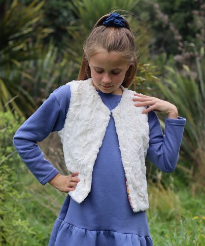 Child wearing the Baby/Child/Teen Honu Vest sewing pattern from Below the Kōwhai on The Fold Line. A vest pattern made in medium-heavy weight cotton, fleece or wool fabrics featuring a straight hem, straight front edges, V-neckline, and single hook and eye closure