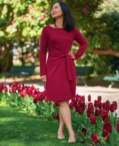 Woman wearing the Tustin Dress sewing pattern from Itch to Stitch on The Fold Line. A dress pattern made in interlock, ponte, cotton Lycra jersey or double-brushed poly fabrics, featuring a waist tie that emerges from the centre front, full length sleeves, boat neckline, and knee length hem.