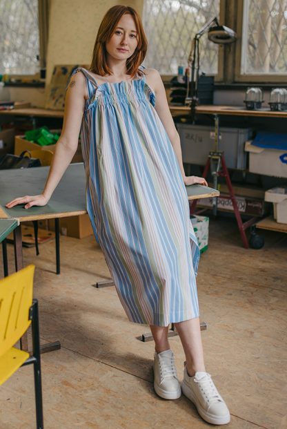 Woman wearing the Evie Dress sewing pattern from JULIANA MARTEJEVS on The Fold Line. A dress pattern made in cotton poplin fabrics, featuring a loose fit, elasticated chest ruffle, shoulder straps that tie, in-seam pockets and midi length.